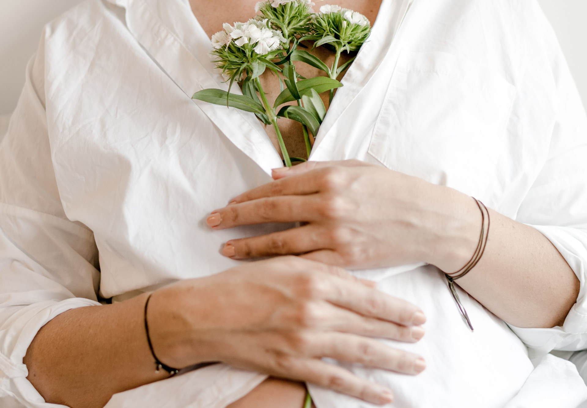 Hands resting over a white shirt with delicate white flowers, a quiet moment of hope on the fertility journey