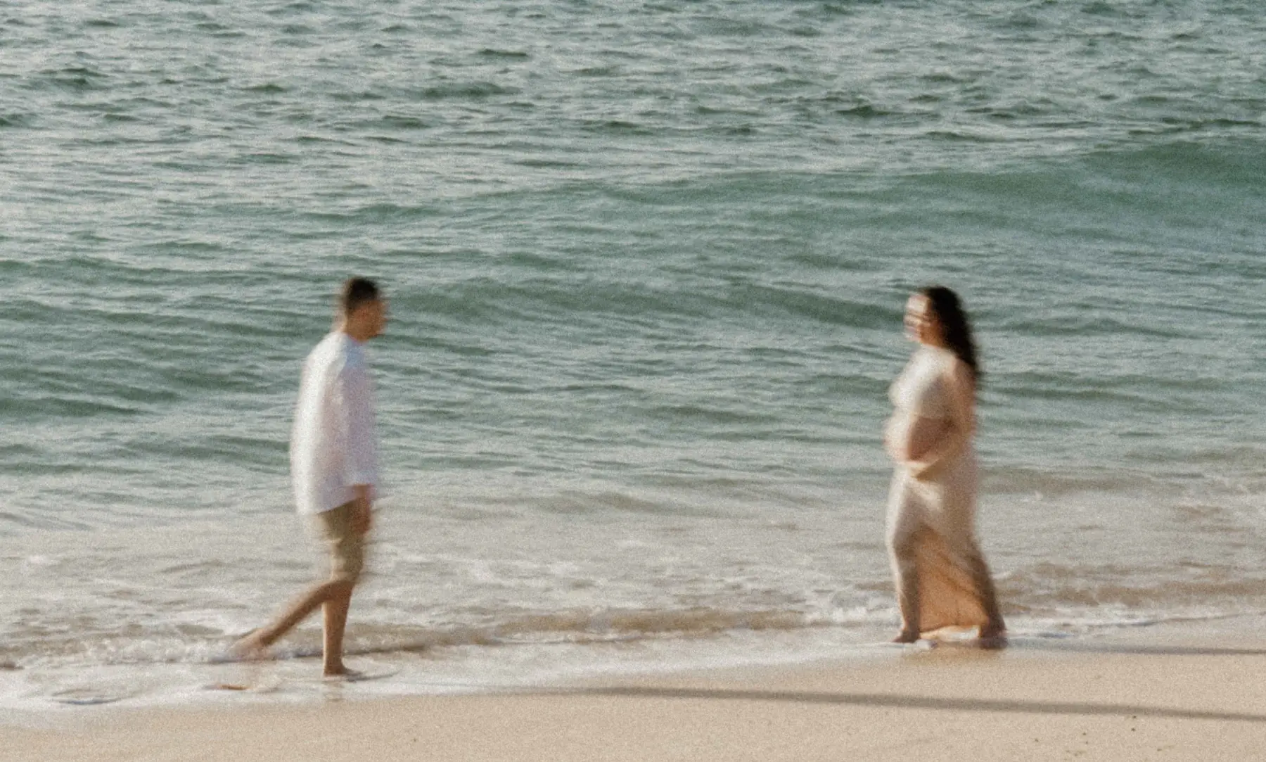 Warm-washed beach shoreline at golden hour, used as a subtle footer background texture