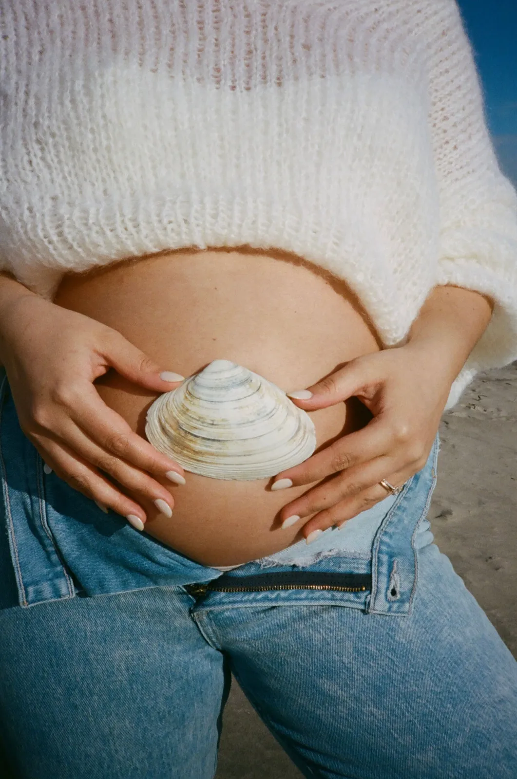 Expectant mother cradling her belly with a seashell resting on it at the beach